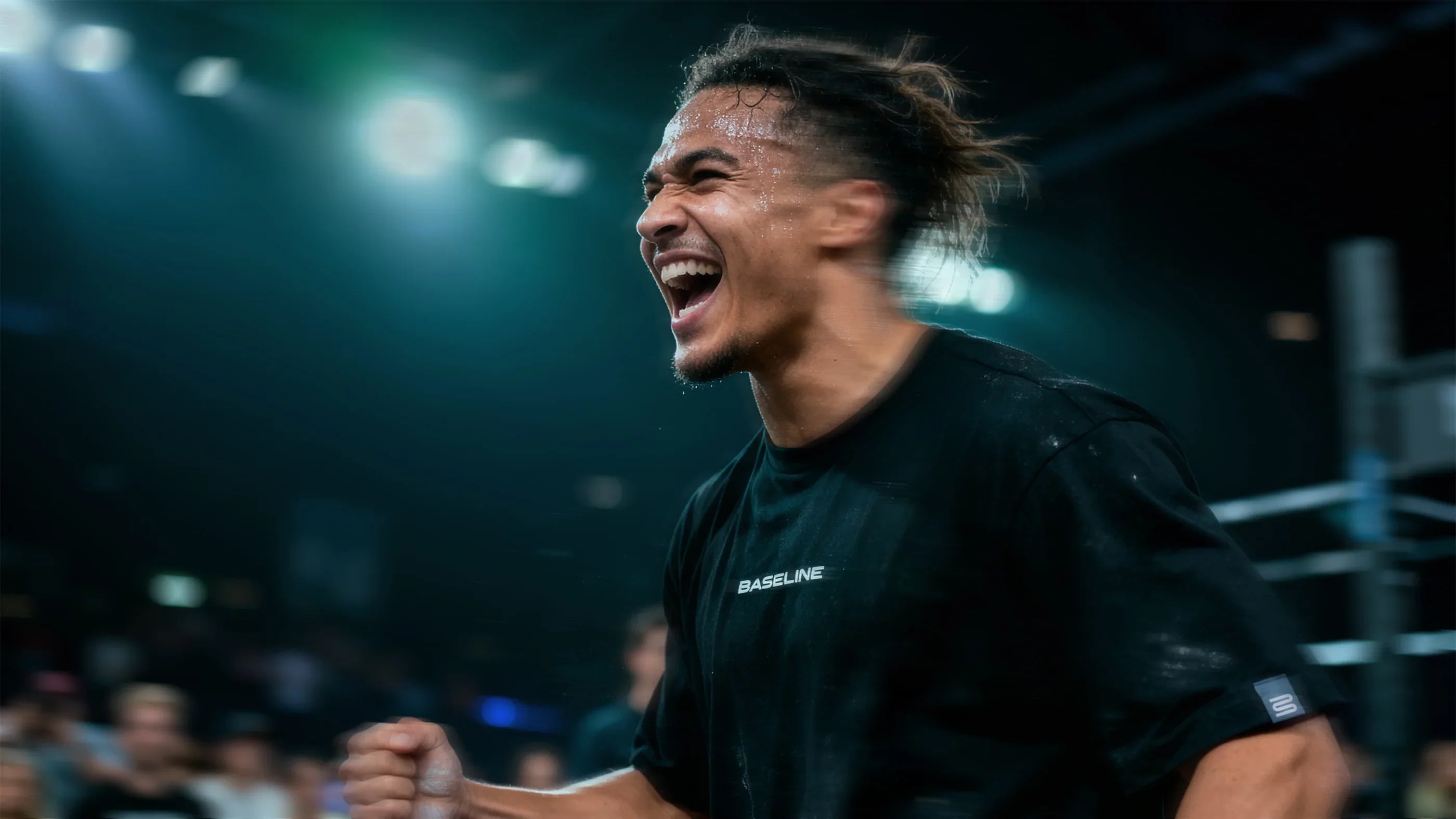 Person in a black shirt with 'BASELINE' branding, celebrating in a darkly lit indoor setting.