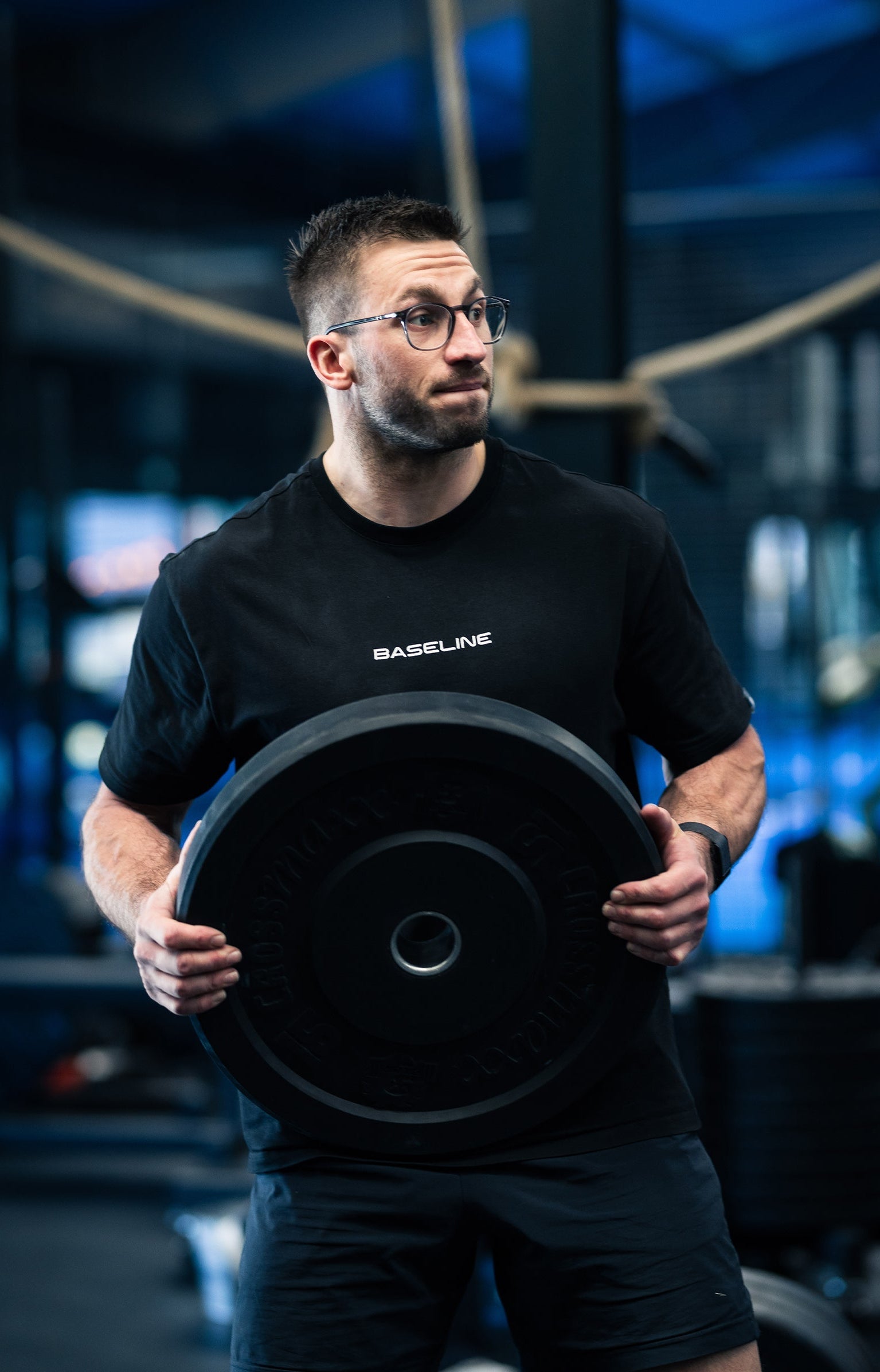 Man holding a black heavy plate in a gym setting