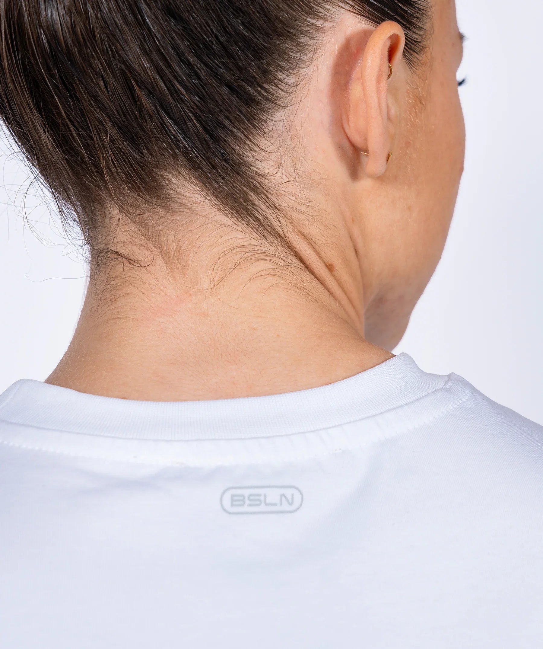 Female athlete wearing a white shirt with a brand logo on a plain background