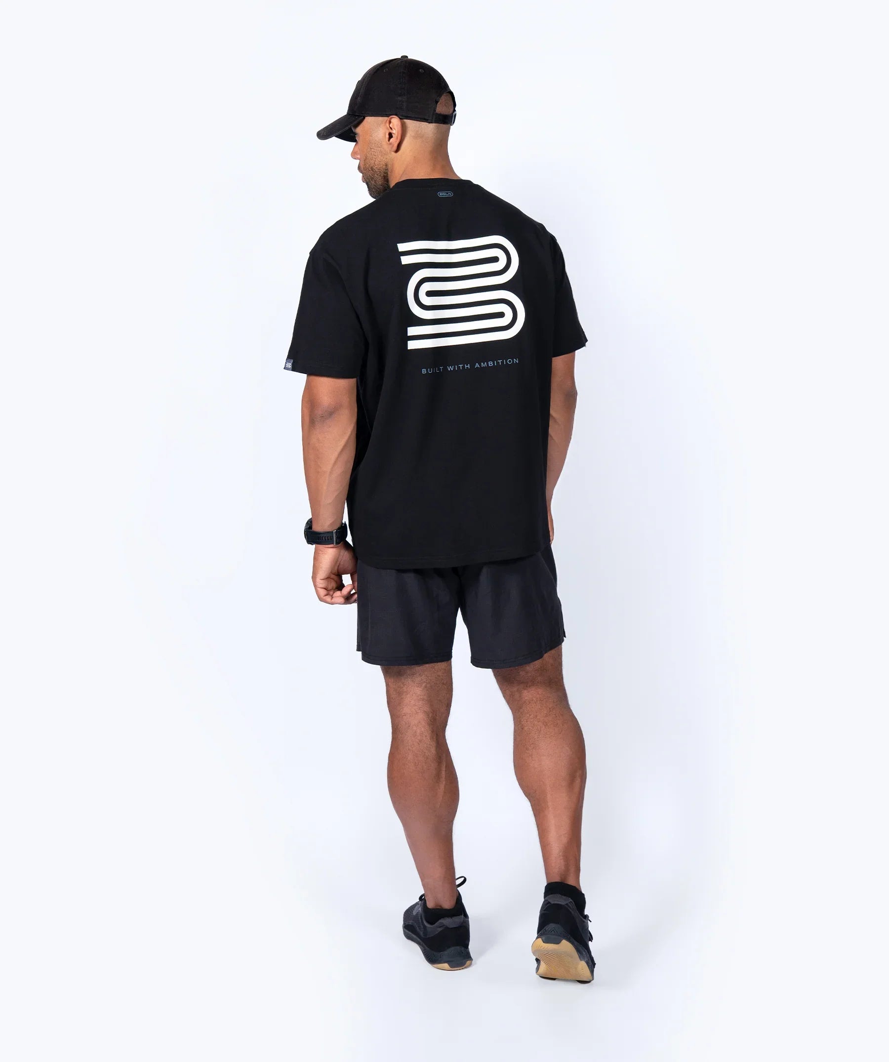 Man wearing a black 'Icon Oversized' t-shirt with a logo on the back, standing against a white background
