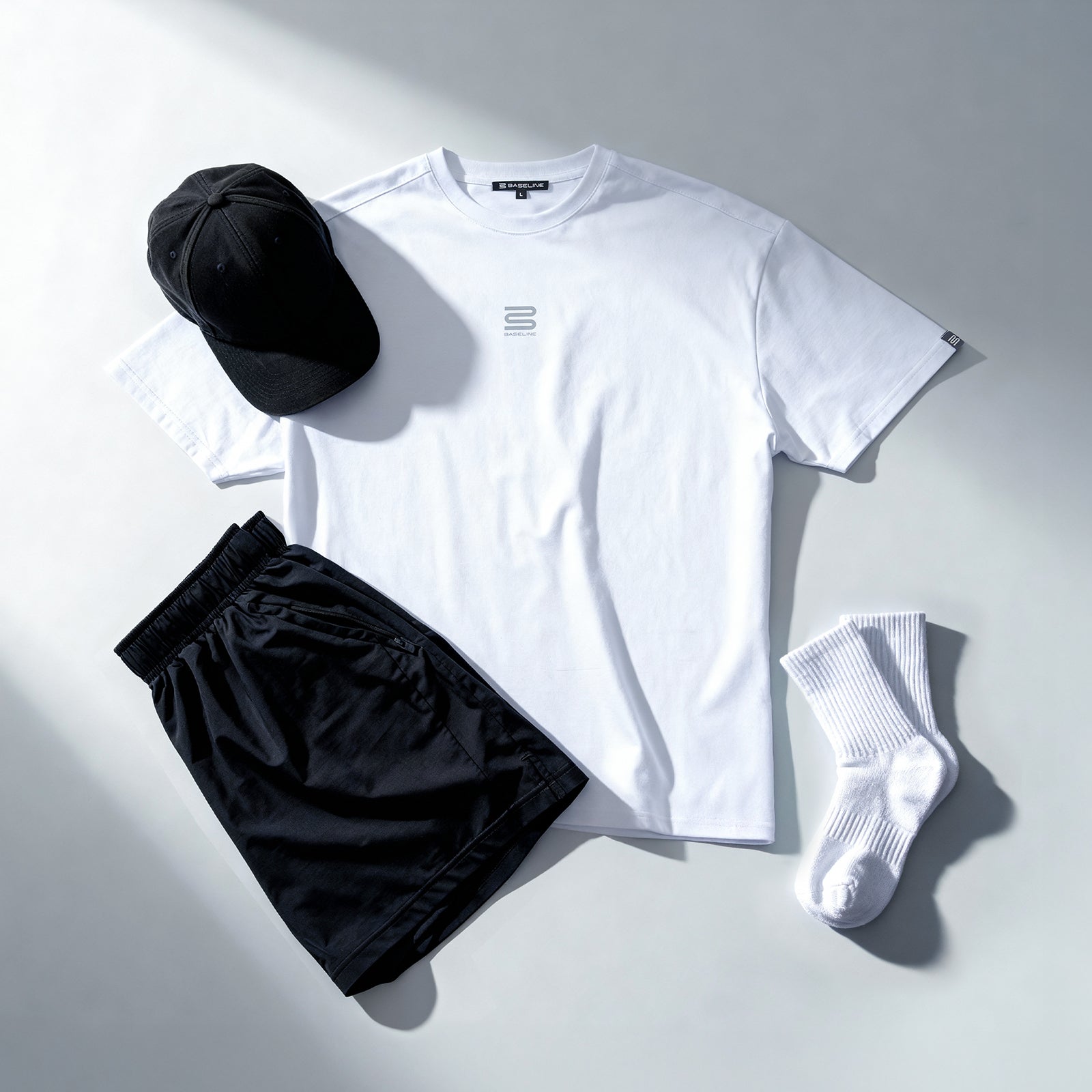 White athletic t-shirt, black shorts, black cap, and white socks laid out on light background