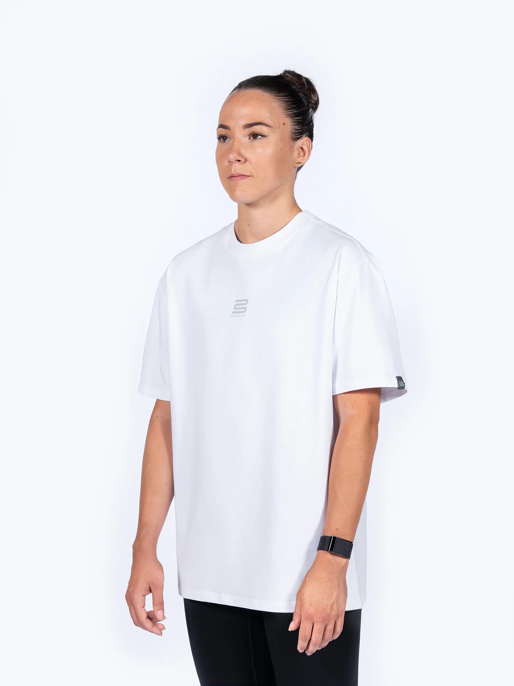 Female athlete wearing a white 'Centric Oversized' t-shirt, facing sideways, on a white background