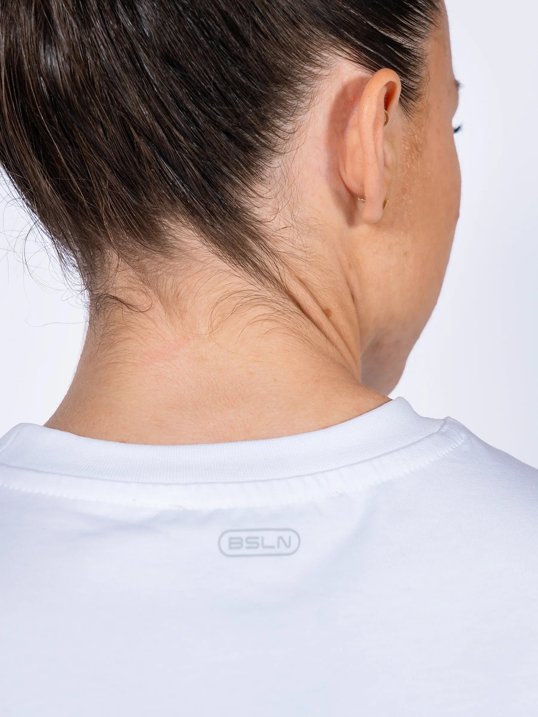 Close-up of a female athlete wearing a white 'Centric Oversized' t-shirt with a brand logo on a light gray background