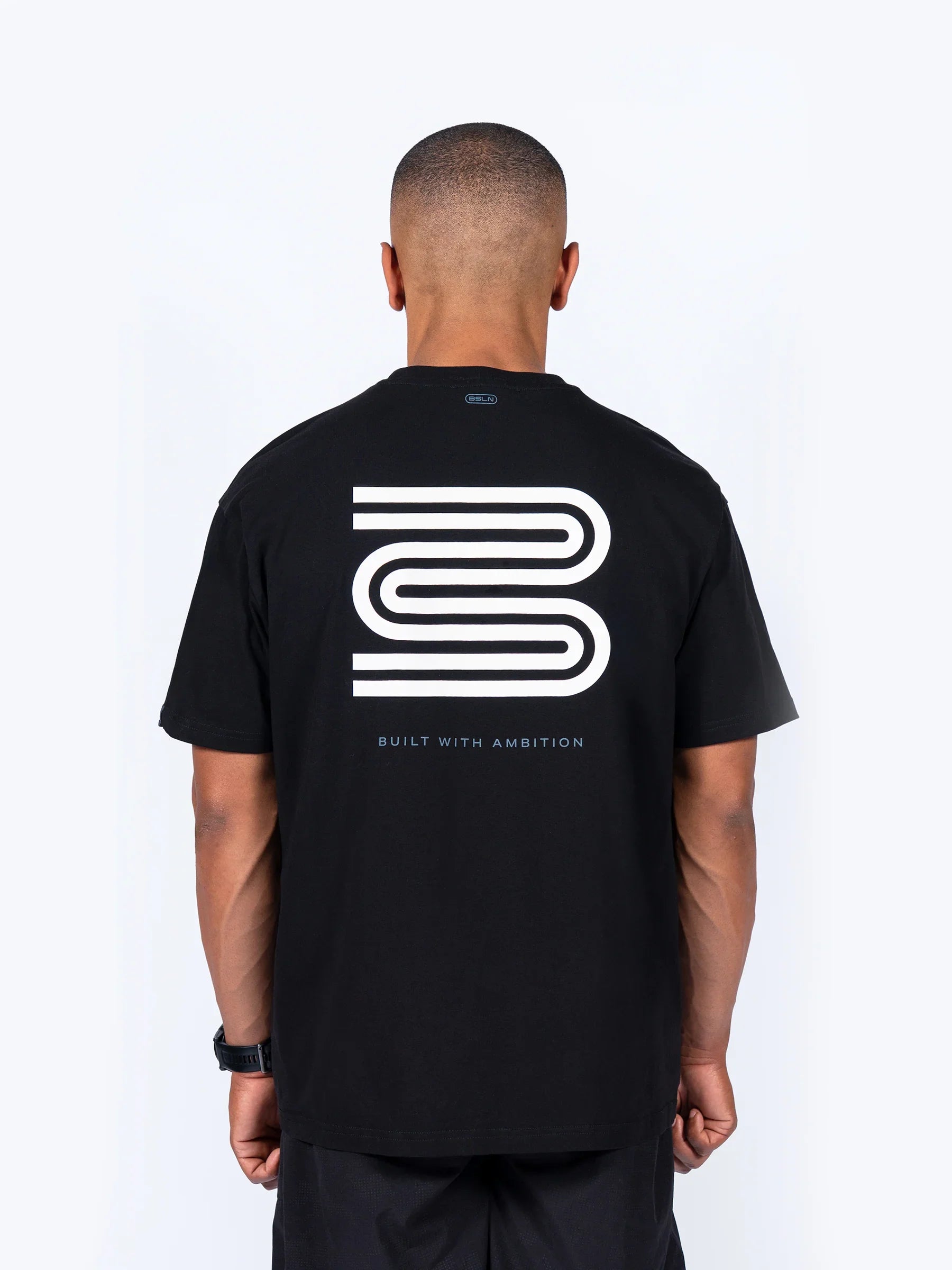 Male athlete wearing a black 'Icon Oversized' t-shirt with a Baseline logo and text on the back against a white background