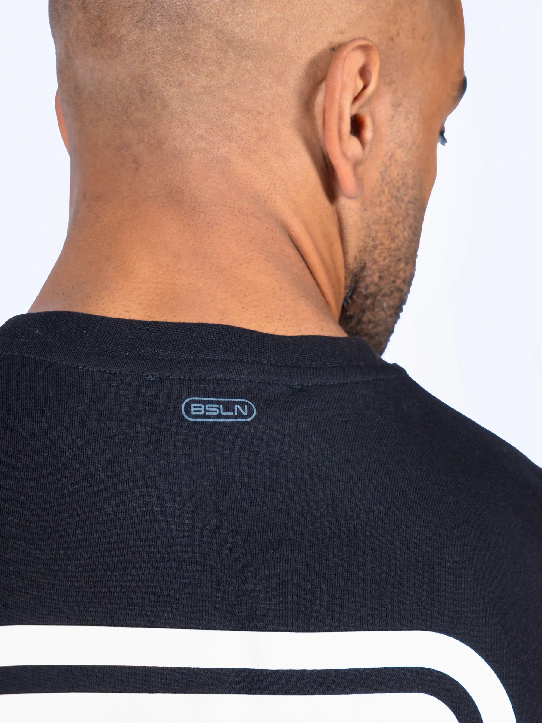 Close-up of a male athlete wearing a black shirt with a logo on the collar against a white background