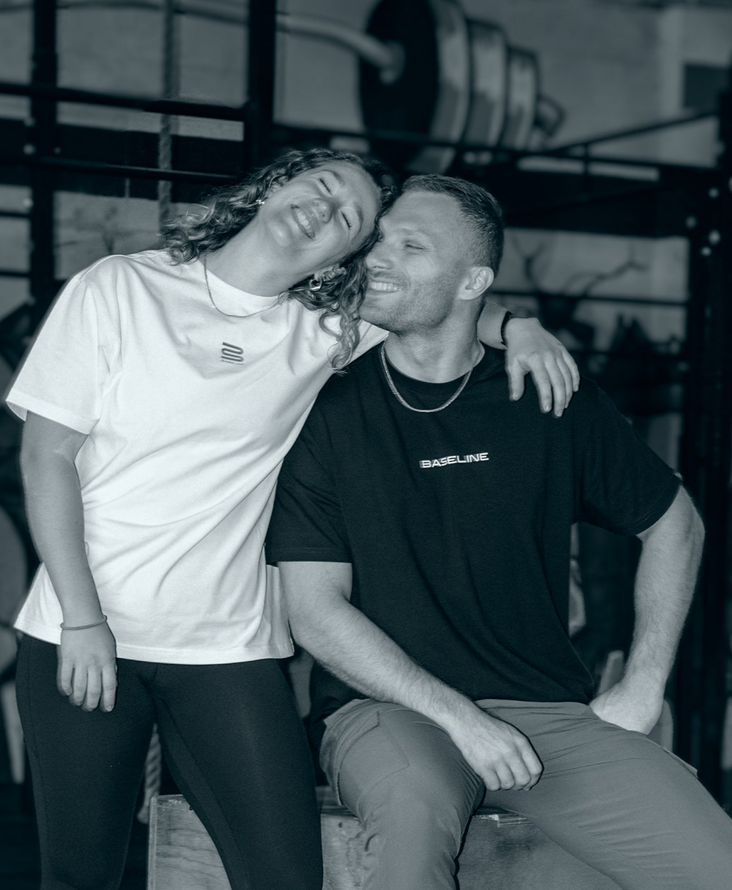 Two people posing together in a casual setting both wearing a 'Baseline' shirt.