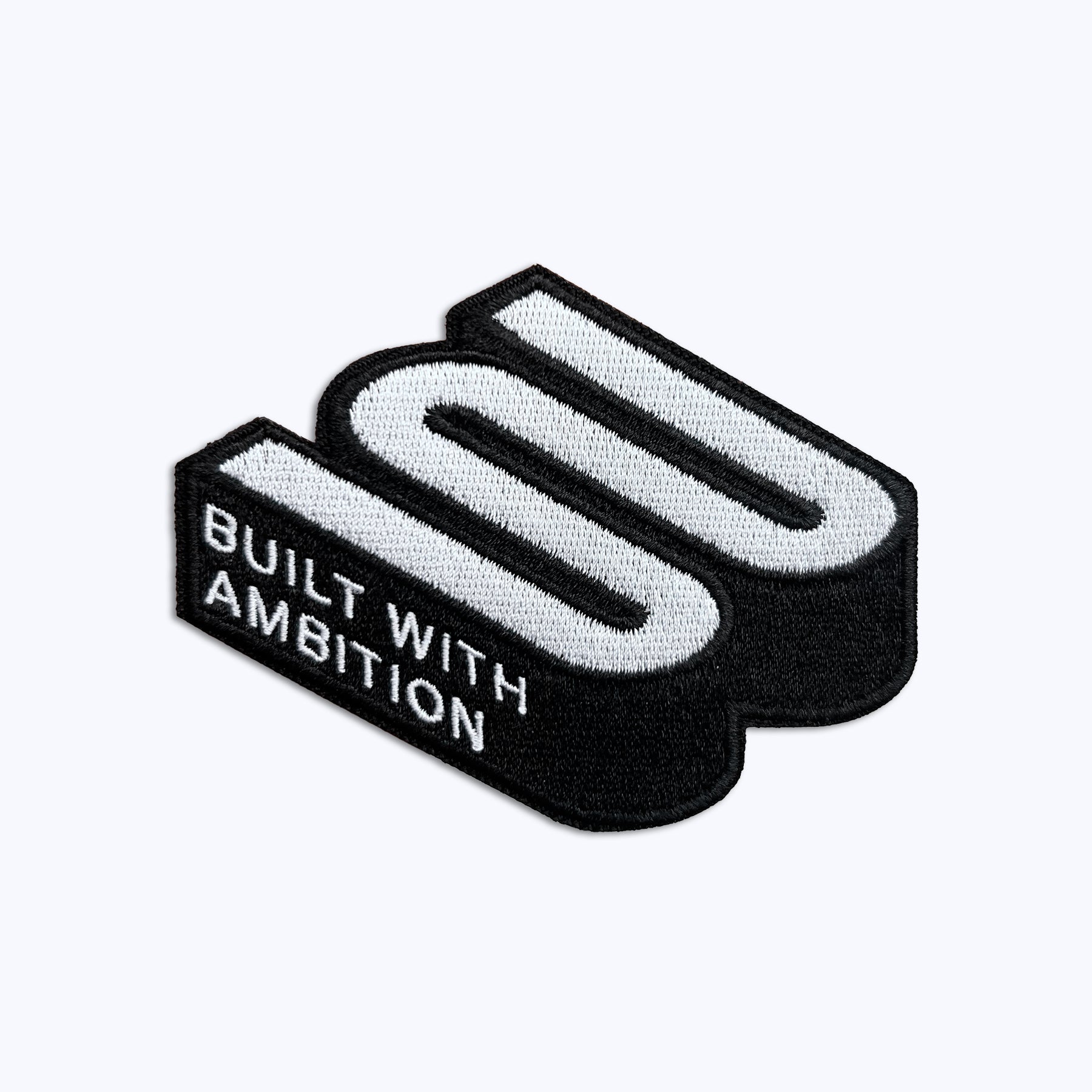 Embroidered patch with 3D logo and text 'Built With Ambition' on white background